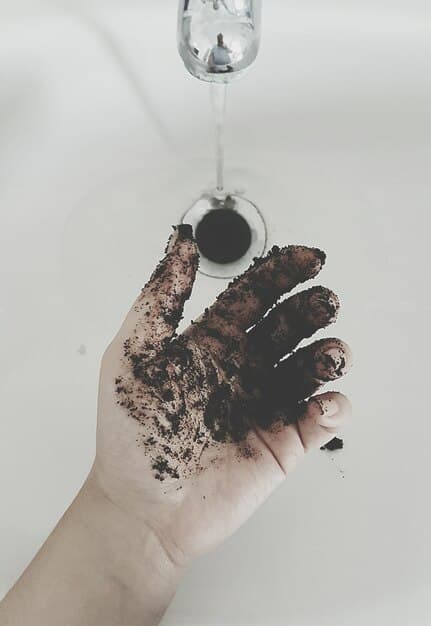 A hand testing the moisture of compost, with droplets of water visible but not dripping. The compost looks rich and dark.