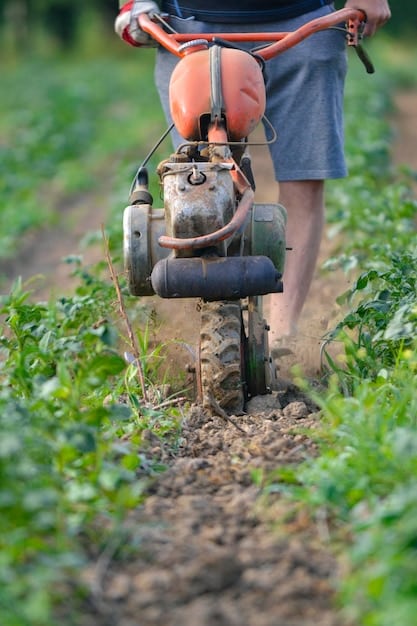 A farmer using a mechanical hoe in a field, showing the tool effectively removing weeds around crop plants. The backdrop features neat rows of crops and well-maintained soil.